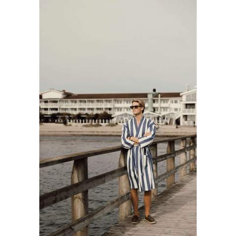 Apportez ce peignoir de hammam doux et confortable à la plage ou profitez-en simplement à la maison. Fabriqué dans un mélange léger et aéré de 200 g/m², il allie le confort du coton aux avantages du séchage rapide du polyester. Conçu dans un style classique avec un motif rayé bicolore, il présente un col soigné, des poches sur le devant, des manches 3/4 et une ceinture à la taille pour un ajustement parfait. Certifié par GRS (Global Recycled Standard), la certification GRS garantit que l'ensemble de la chaîne d'approvisionnement des matériaux recyclés est certifiée. Le contenu recyclé total est basé sur le poids total du produit. Ce produit contient 69 % de coton recyclé certifié GRS et 29 % de polyester recyclé certifié GRS.